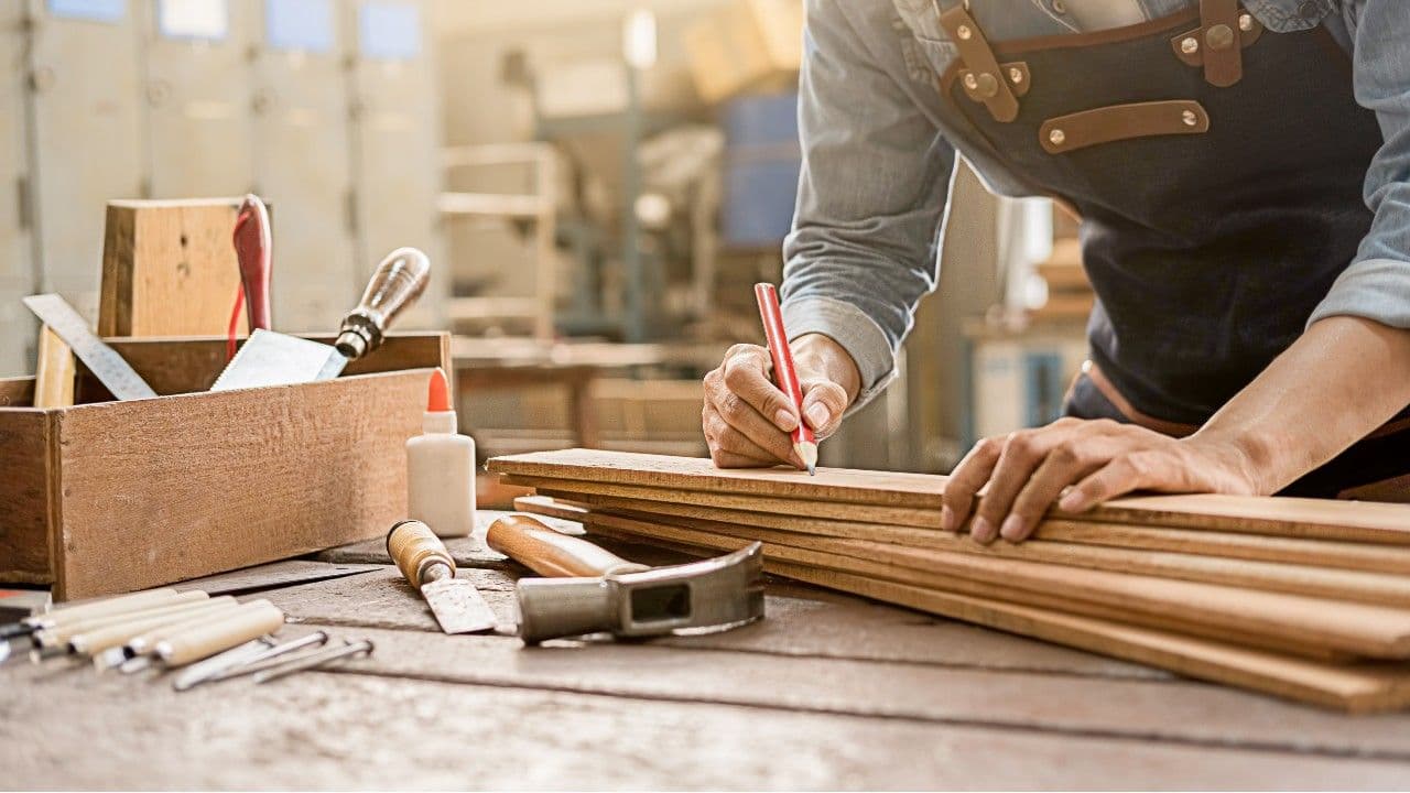 Manos midiendo sobre una tabla de madera con lápiz y regla, asegurando precisión en cada corte.