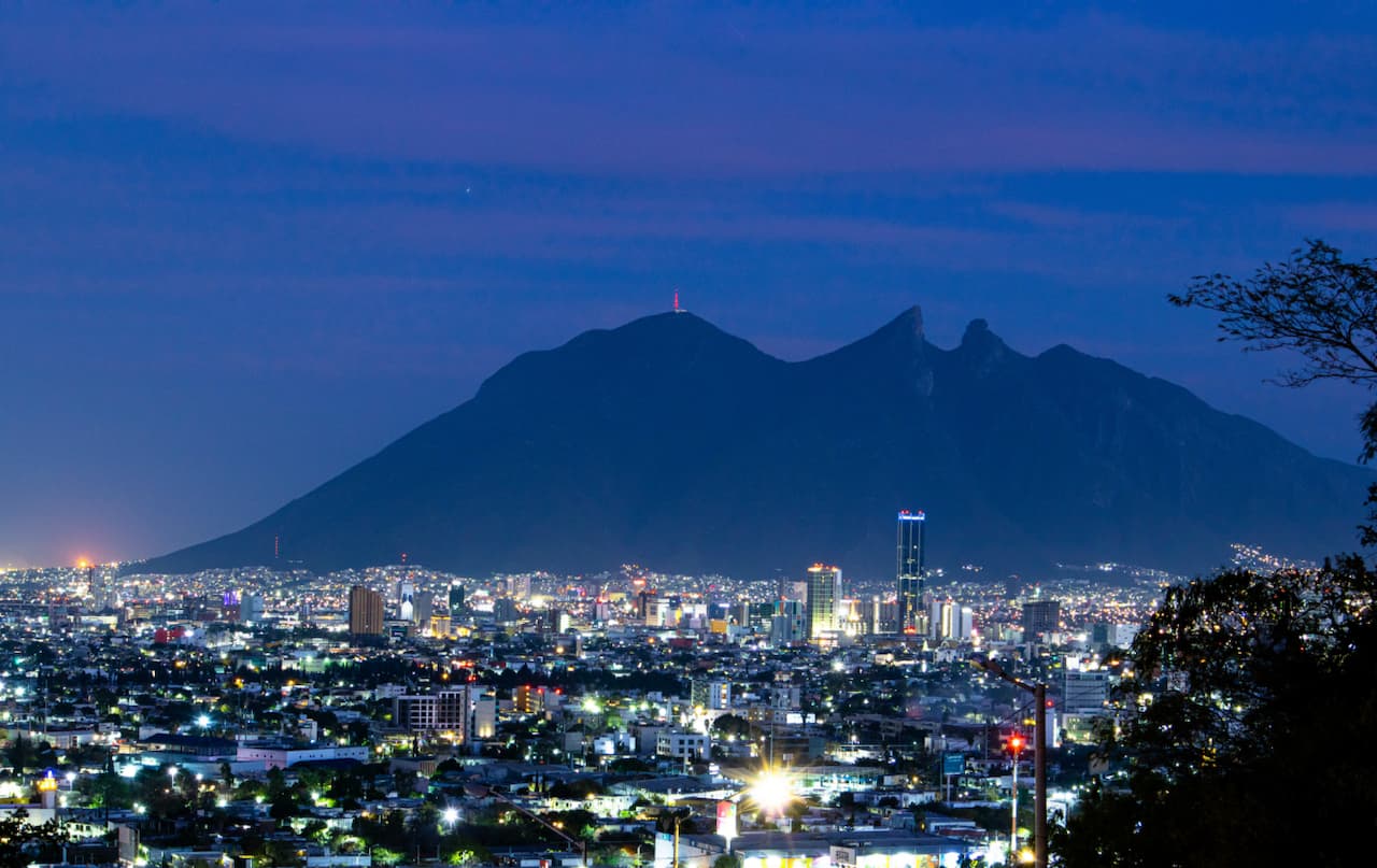 Vista nocturna de Monterrey con el Cerro de la Silla iluminado en el horizonte.
